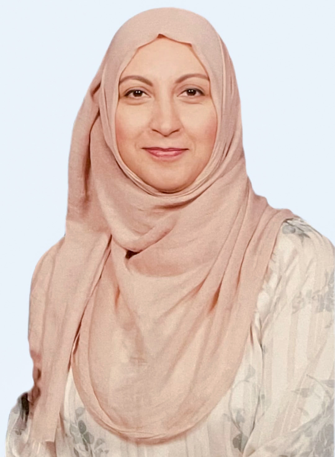 A woman wearing a light pink hijab and a light-coloured, patterned top smiles softly against a plain, light background.